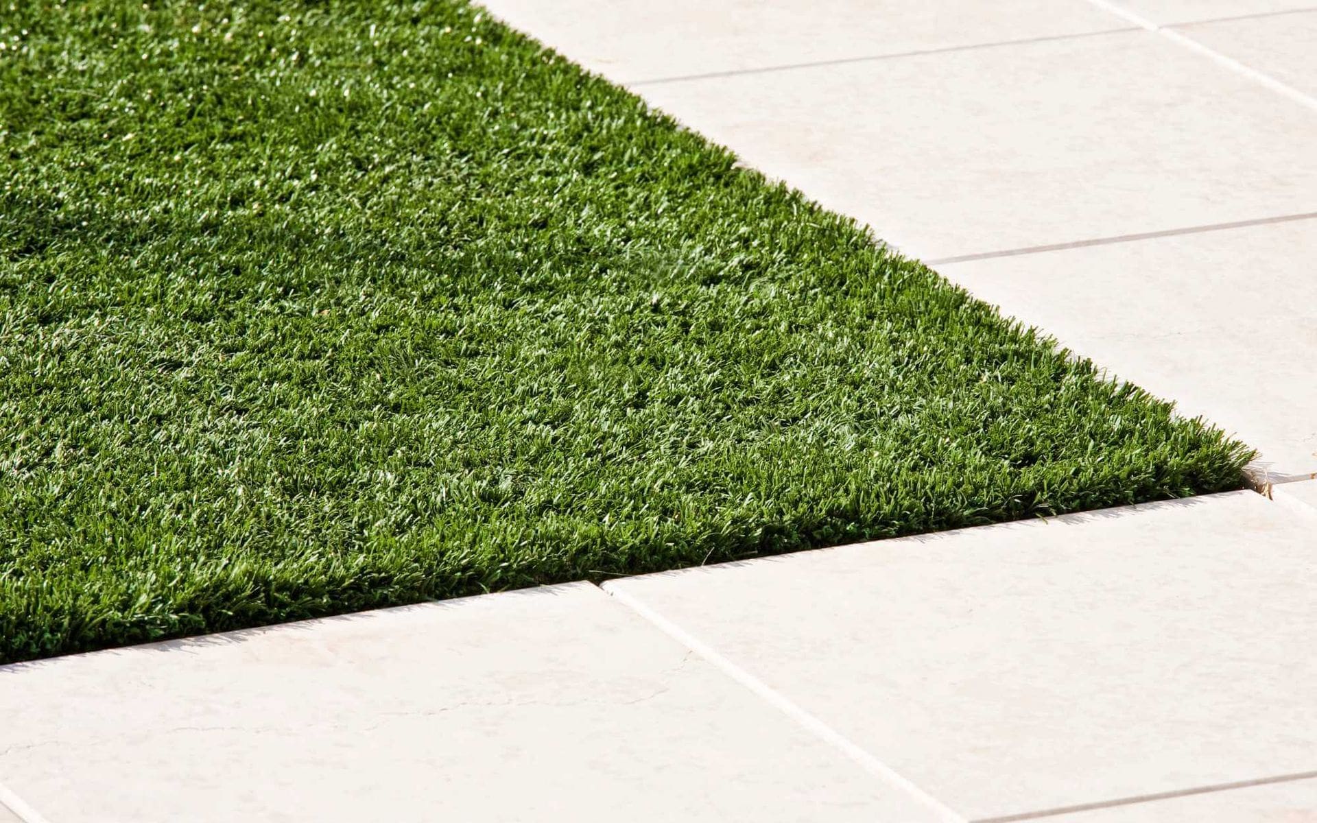 A close-up view of a neatly cut green lawn adjacent to white, tiled flooring. The contrast between the lush grass's texture and the smooth, light-colored tiles is clearly visible. West Valley Concrete specializes in creating such seamless transitions with decorative concrete designs.